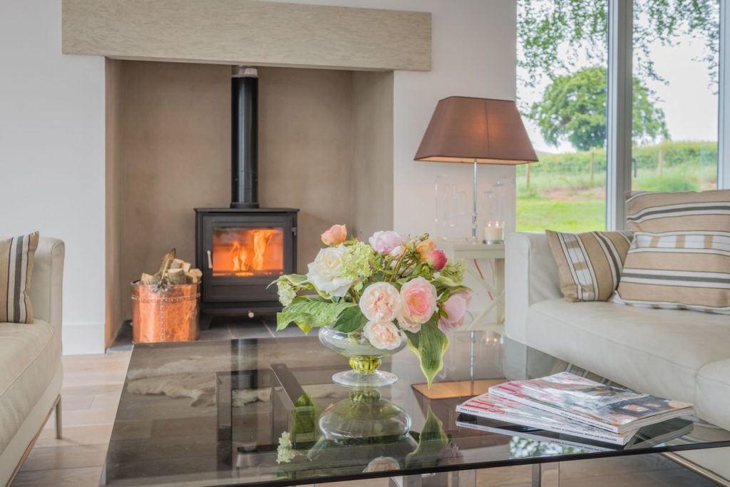 Glass coffee table with vase of flowers in front of log burner
